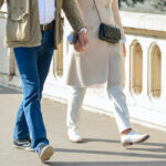 Couple seen from the waist down holding hands and walking across a bridge in Europe