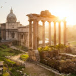 Sun shining over marble columns and a domed stone building in the Ancient Forum of Rome, one of the best family vacations with teens