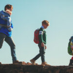 A man carrying a small child walking in line behind two other children wearing backpacks