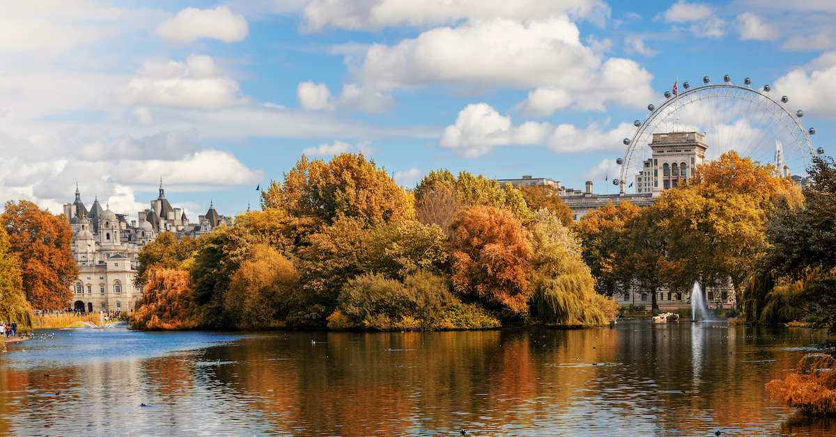 Pond in the foreground with a castle and ferris wheel rising out of autumn trees in the middle ground in St. James Park, London, one of the best places in Europe to visit with kids