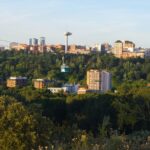 Cable car glides above the greenery of Casa de Campo with Madrid city buildings such as Plaza Mayor in the distance