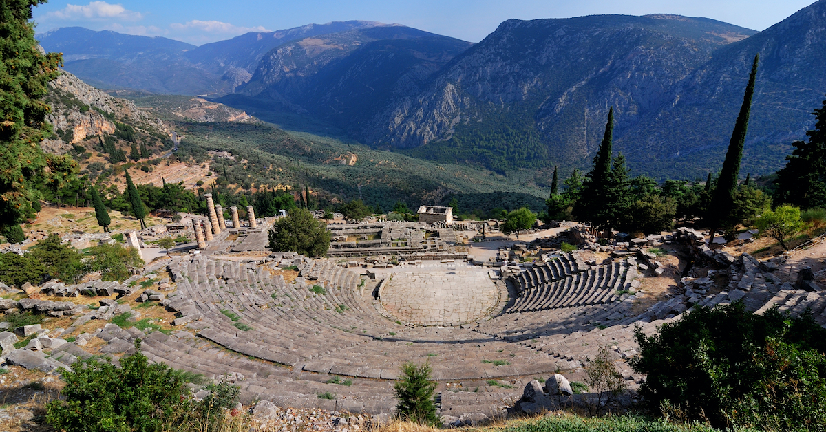 The amphitheater of Delphi in the foreground with the Temple of Apollo in the middle ground and mountains in the background