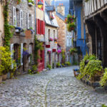 Cobblestone street lined with stone buildings and pots filled with colorful plants and flowers