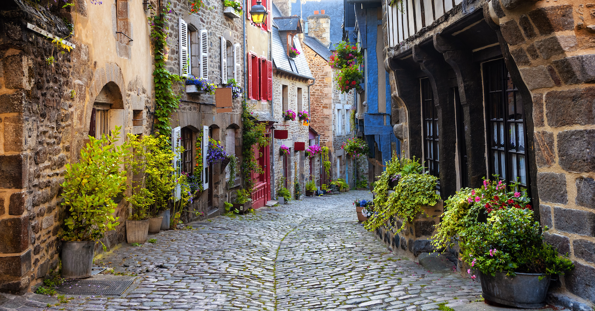 Cobblestone street lined with stone buildings and pots filled with colorful plants and flowers
