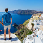 Young couple looking out over the white-washed buildings along the caldera in Oia, Santorini, one of the most popular Greece honeymoon destinations