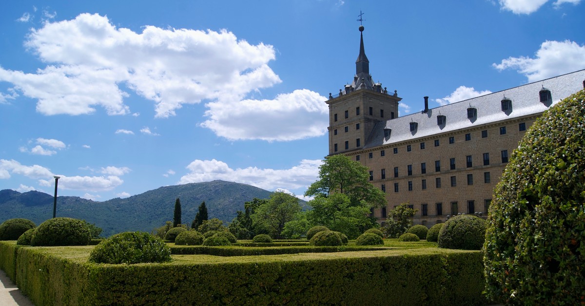 Maze-like hedges of Jardin de Los Frailes in the foreground with the massive beige monastery of San Lorenzo de El Escorial in the background