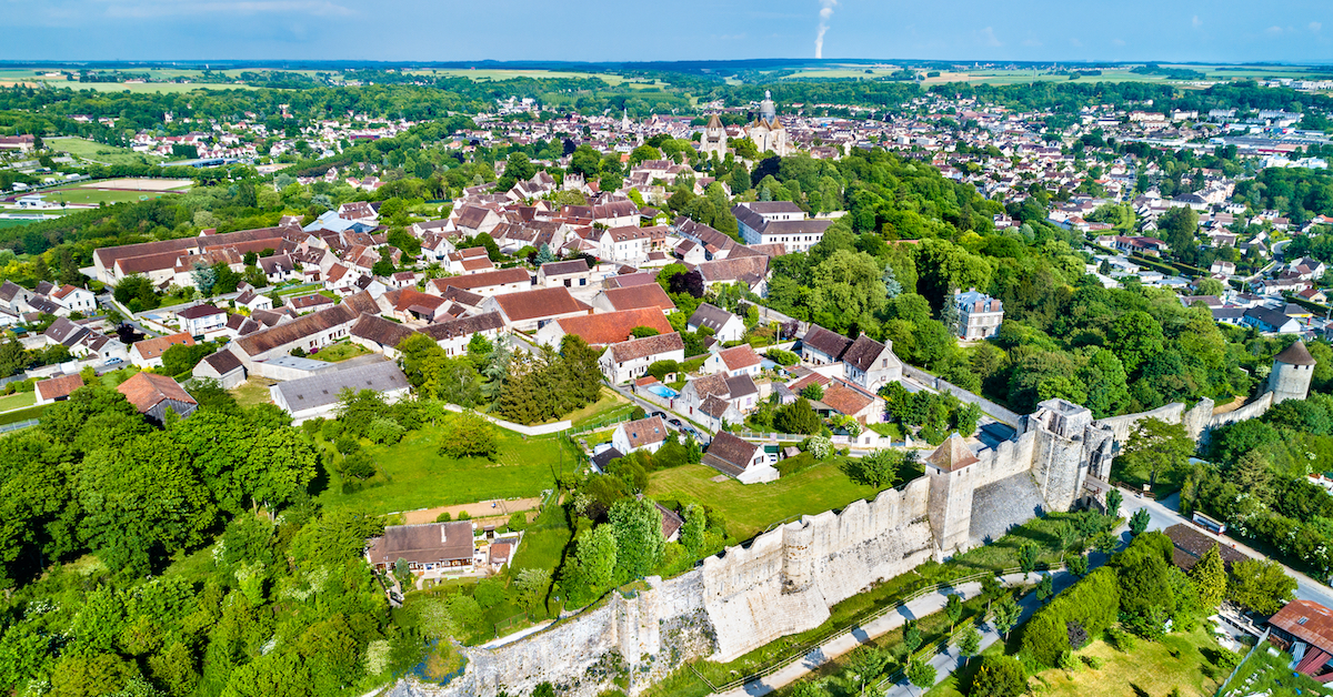 Aerial view of the small city of Provins, France with a large wall forming a boundary along one side and greenery and stone buildings in the center