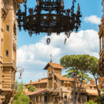 Metal chandelier hanging from an archway leading to the intricate stone buildings of Quartiere Coppede in Rome, Italy