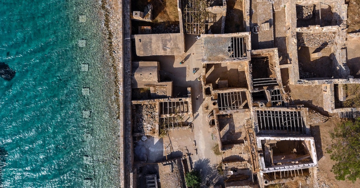 Aerial view of Spinalonga with blue ocean on the right and fortress ruins on the left