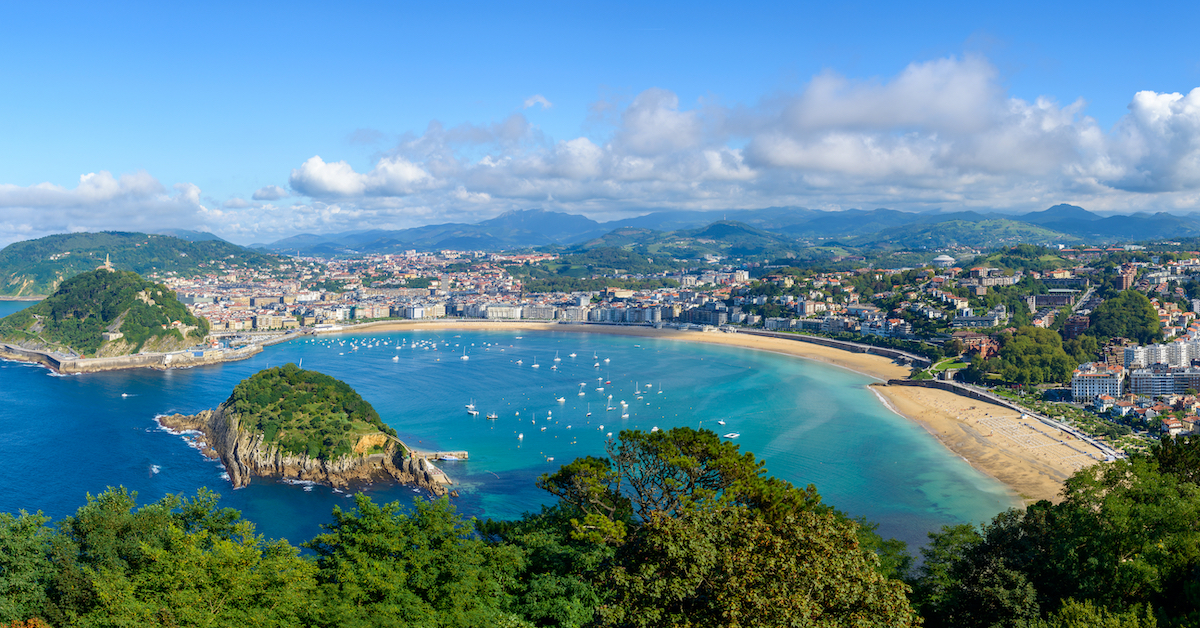 Aerial view of the city of San Sebastian and its beaches lining Concha Bay with a rocky green island in the middle of the water