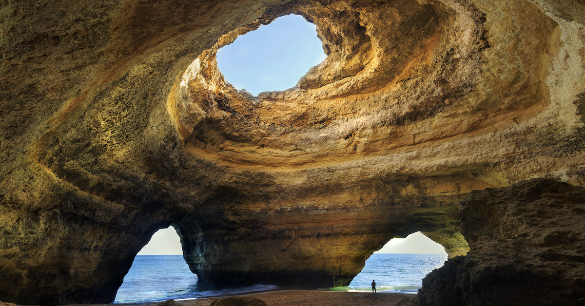 Inside view of the the Algarve’s golden Benagil Cave, with a hole in the ceiling shining light in and two more holes at the base allowing the ocean in