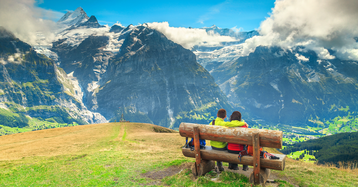 Young couple sitting on a bench overlooking the snowy mountains and green valleys of the Bernese Oberland, one of the best Switzerland honeymoon destinations