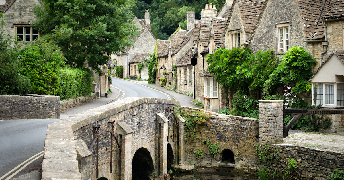 Road over a bridge leading into a street lined with stone cottages in the Cotswolds, one of the most charming United Kingdom honeymoon destinations