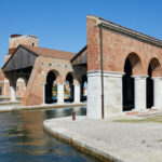 Stone archways lining blue water leading into the Venetian Arsenal