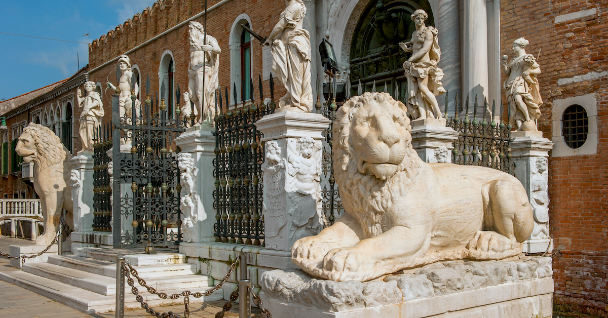 Two marble lion statues in from of the ornate gate of a reddish stone building