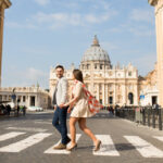 Young couple holding hands crossing the street with the Vatican in the background