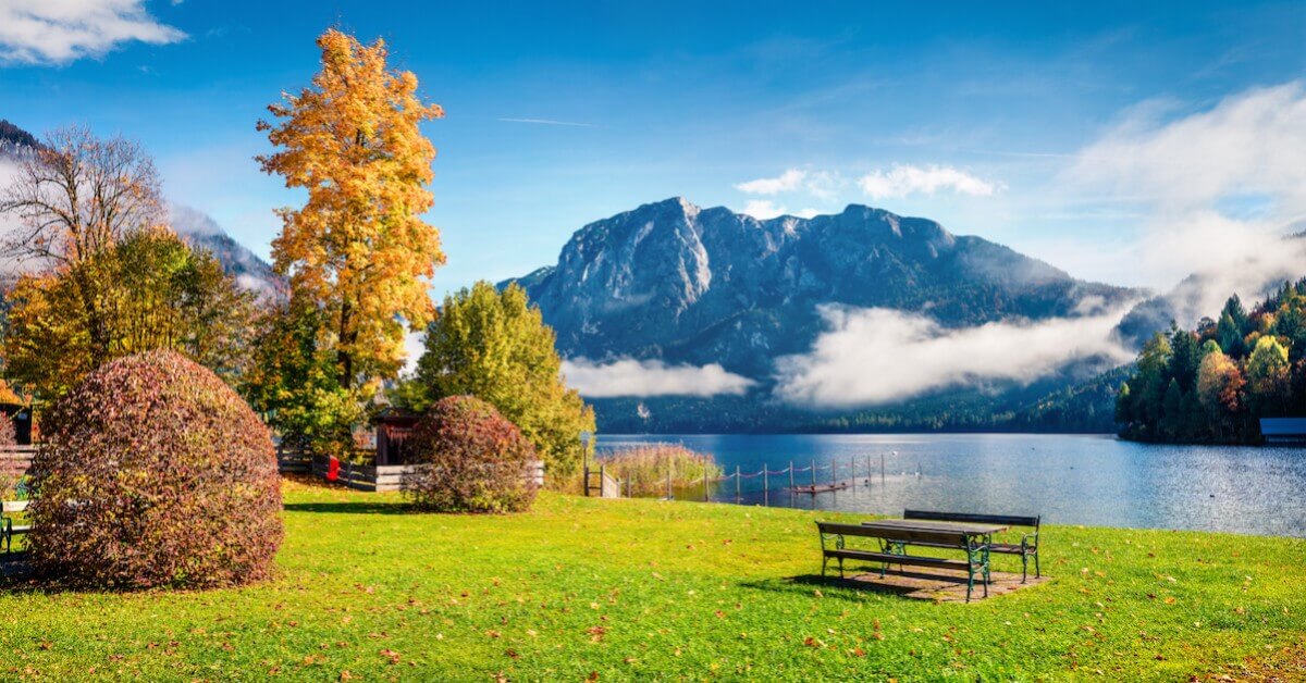 Green grass and fall foliage in the foreground with a lake and mountains in the background in Austria’s Lake District