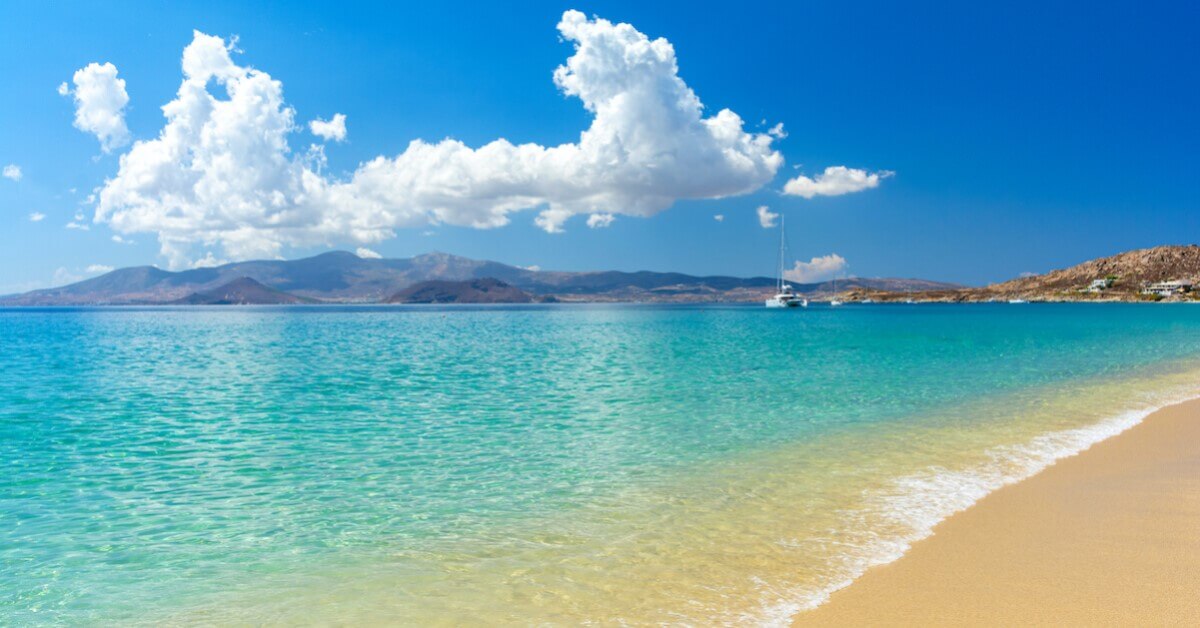 Golden sandy beach on Naxos, Greece with crystal clear water and a boat a rugged land in the distance, perfect for relaxing vacations