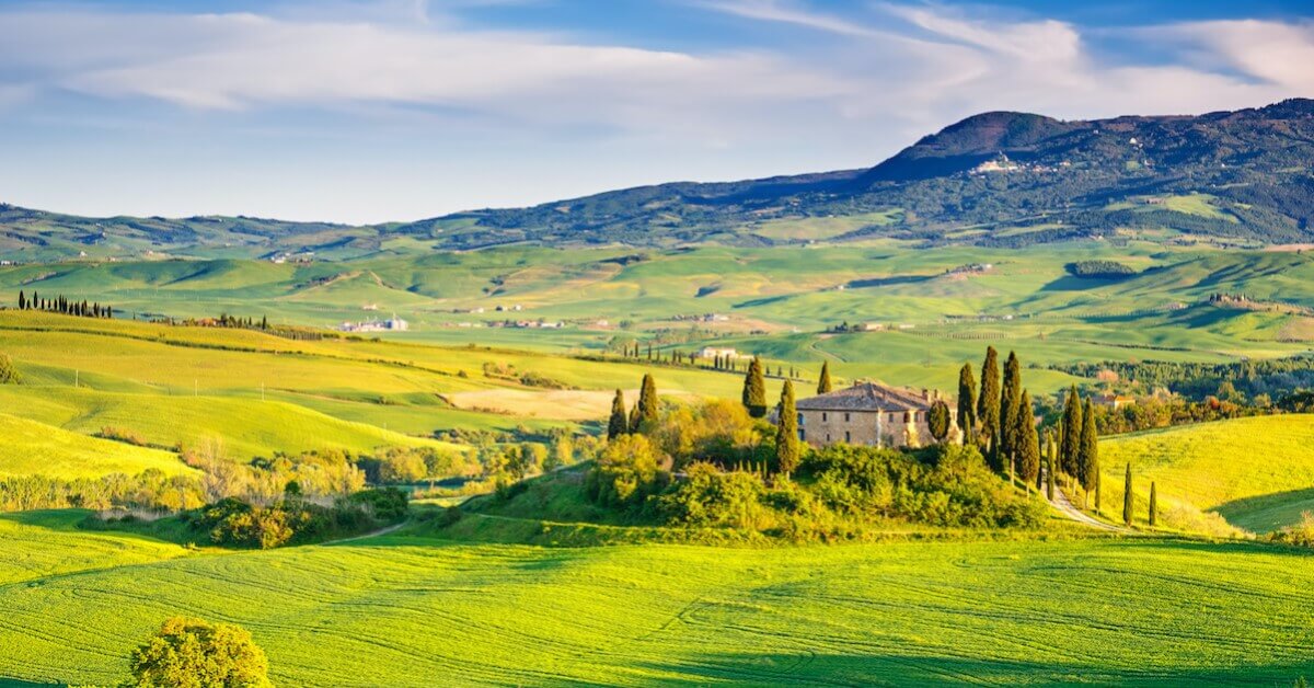 Sprawling view of green hills and cypress trees surrounding a stone villa in Tuscany, one of the most relaxing vacations throughout Europe