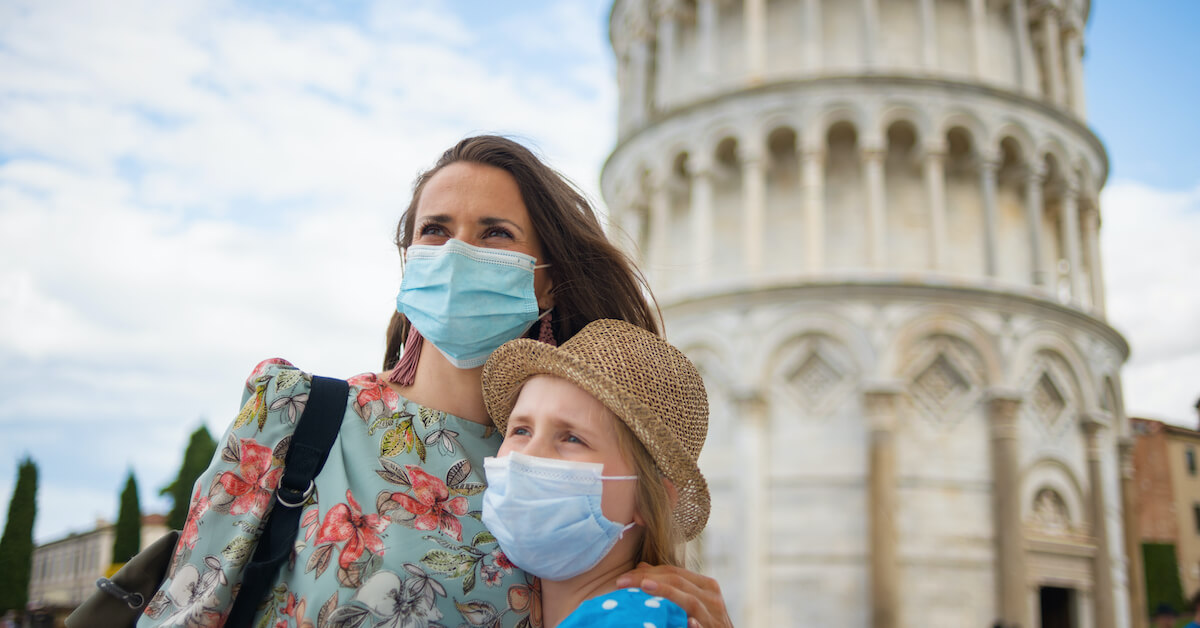A woman and her daughter wearing face masks posing for a photo in front of the Leaning Tower of Pisa in Italy, an adjustment of expectations that is one of the most important post-pandemic travel tips to keep in mind