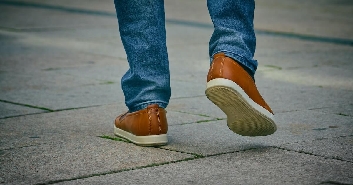 Close up of someone's feet in brown leather shoes walking along a stone path