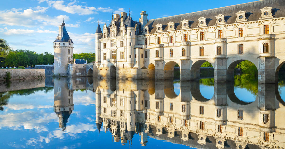 White castle with a blue roof reflecting in the pond below it on a sunny day in the Loire Valley, France