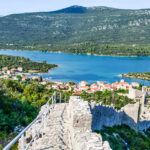 Aerial view of part of the Walls of Ston leading down to town on the water with green mountains in the background