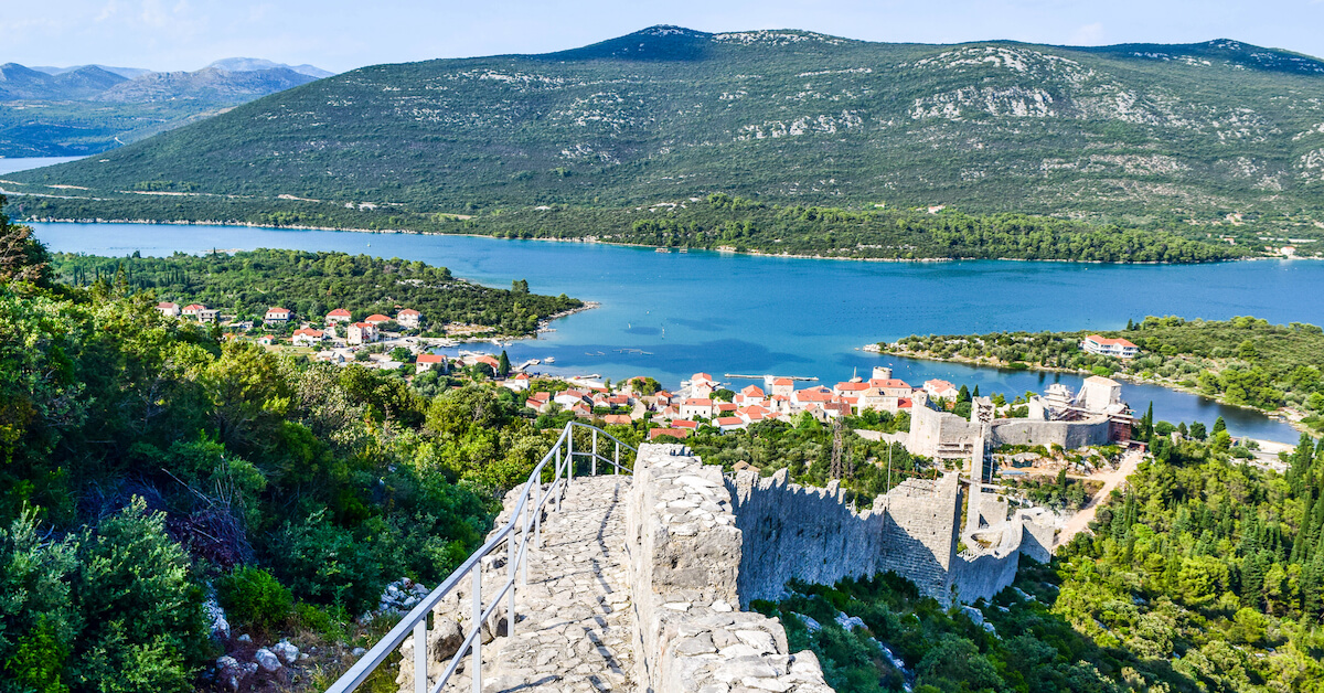 Aerial view of part of the Walls of Ston leading down to town on the water with green mountains in the background