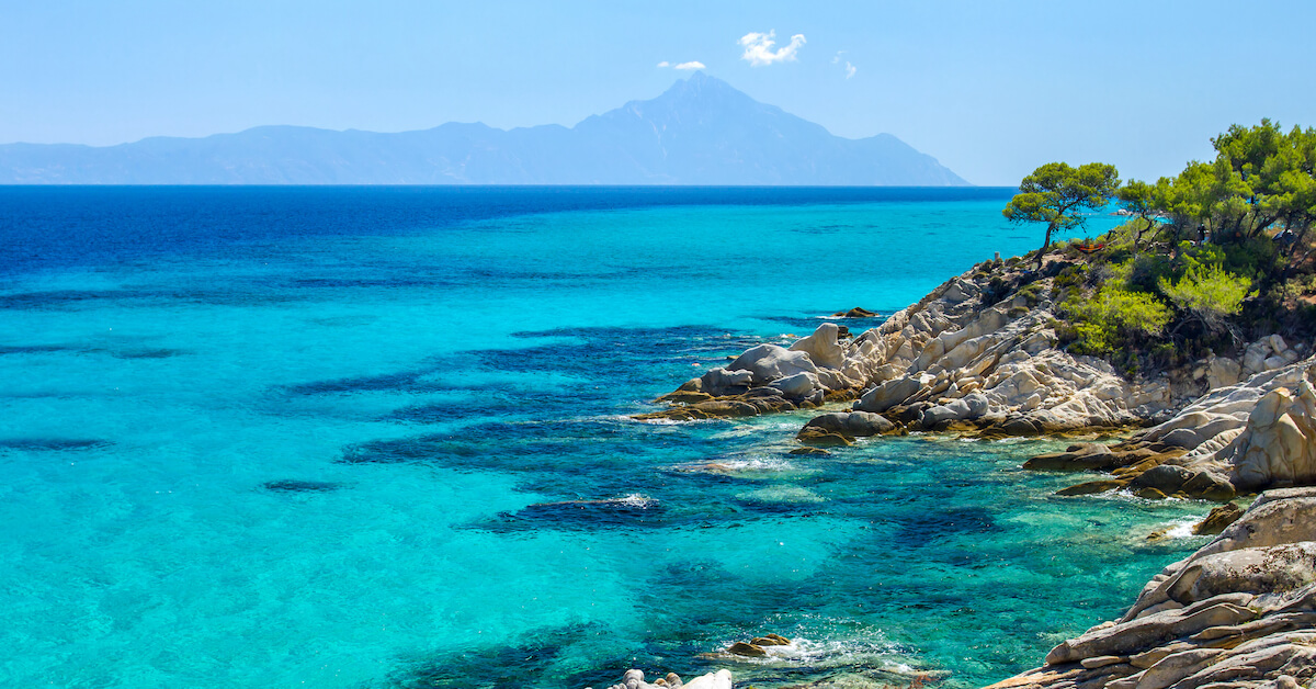 Bright blue waters along a rocky coast with mountains in the distance in Northern Greece