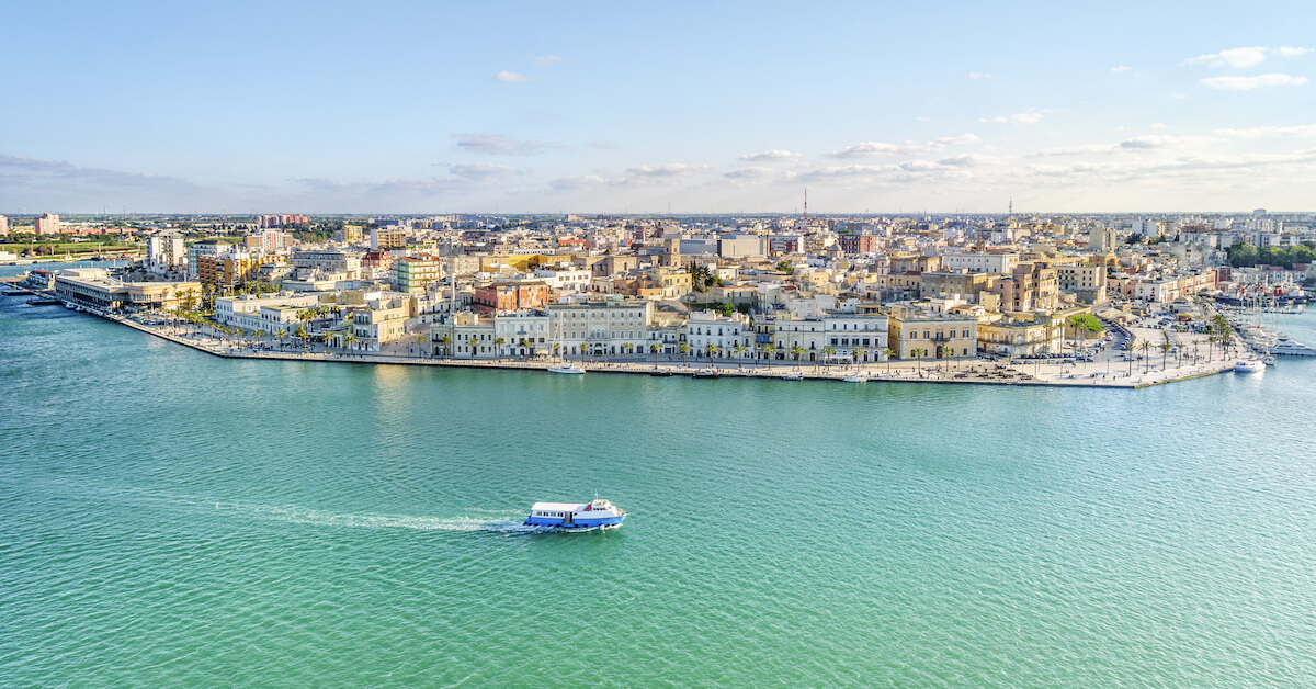 Aerial view of a boat on a clear sea with a city in the background in Puglia, Italy