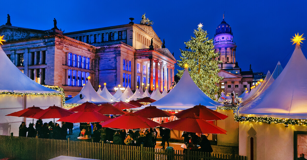 Markets stalls and a Christmas tree in front of elaborate stone buildings at night