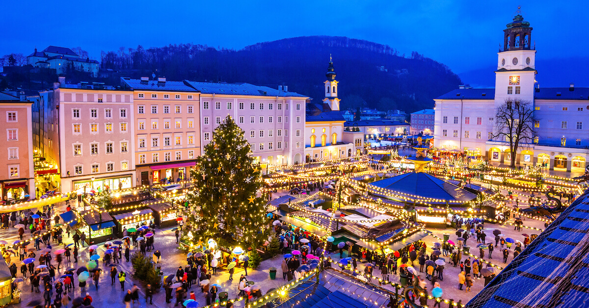 Aerial view of a city square full of market stalls, string lights, and a Christmas tree at night