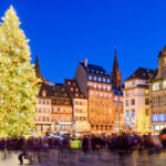 A busy city square with a Christmas tree at night