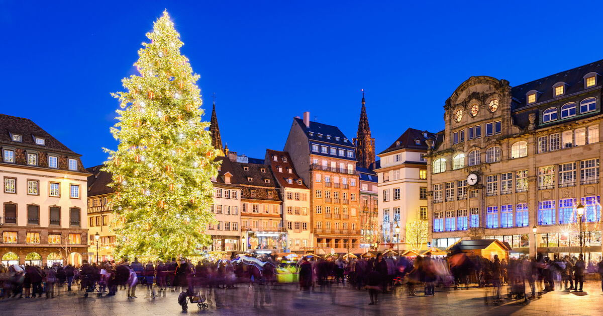 A busy city square with a Christmas tree at night